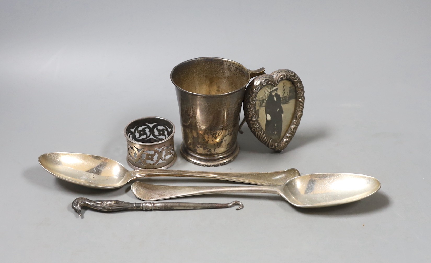Two 18th century silver spoons, a later silver christening mug, small silver mounted heart shaped photograph frame, a silver napkin ring and a silver handled button hook.